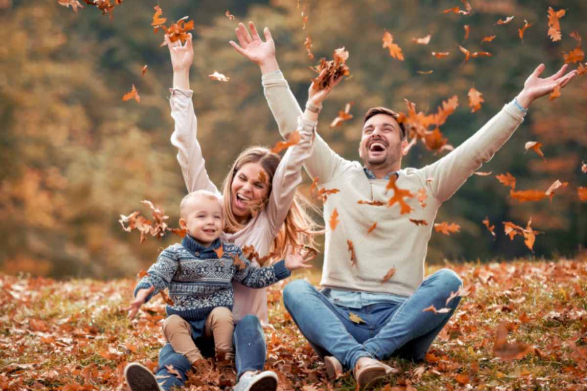 genitori con bambino che esultano seduti sopra delle foglie secche