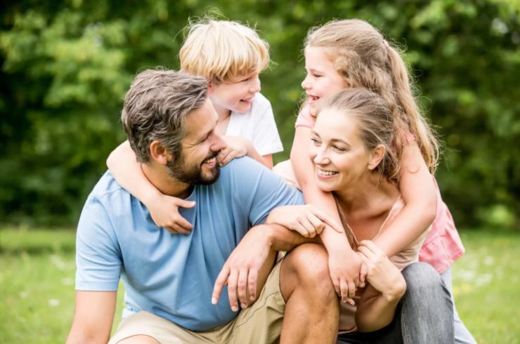 genitori sorridenti che portano un bambino e una bambina sulle spalle