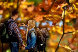 foglie d'autunno e coppia in gita che fa un cuore con le mani