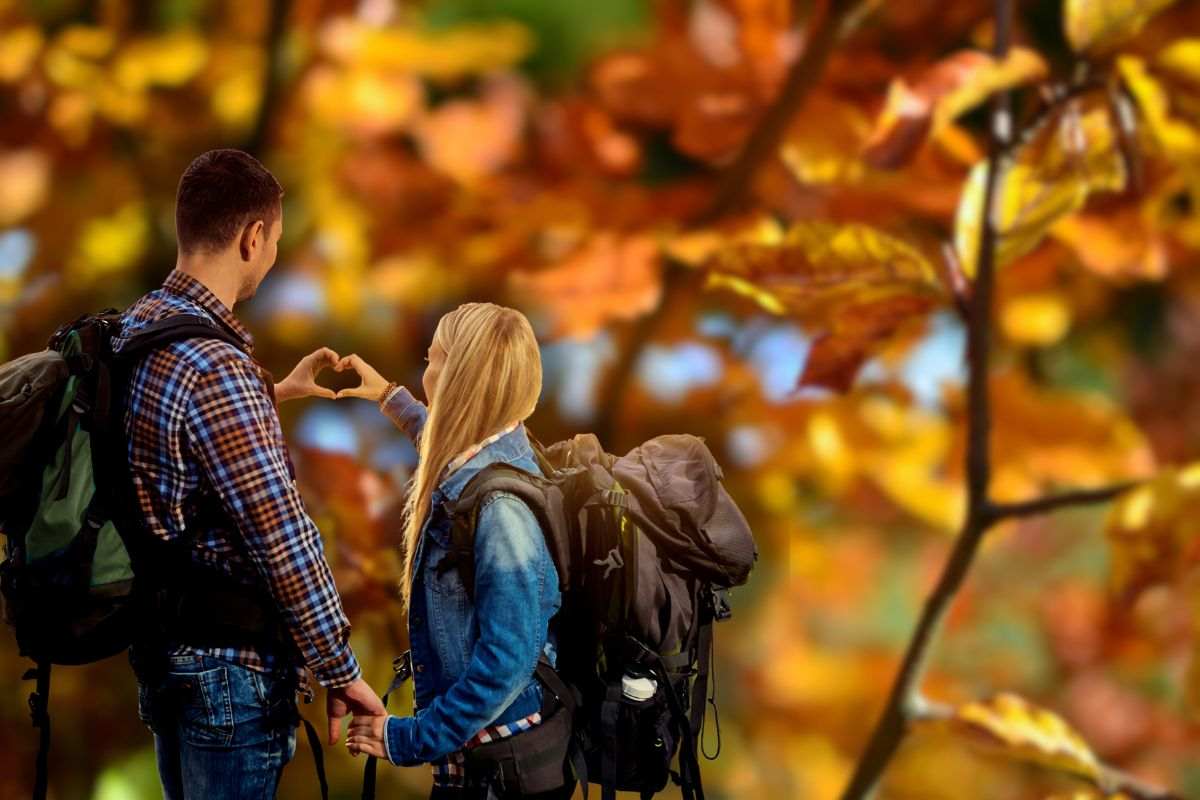 foglie d'autunno e coppia in gita che fa un cuore con le mani