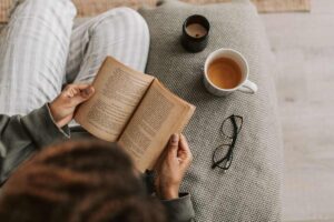 Una persona che legge un libro su un divano vicino ad una tazza di caffè