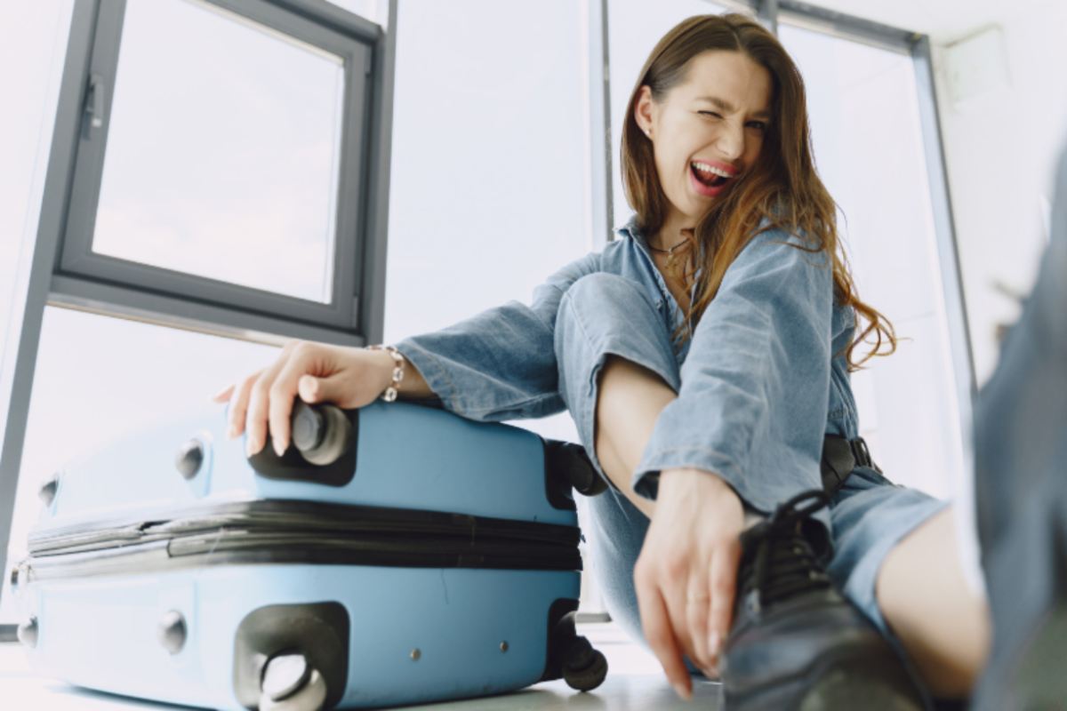 donna che fa l'occhiolino seduta per terra accanto ad un trolley