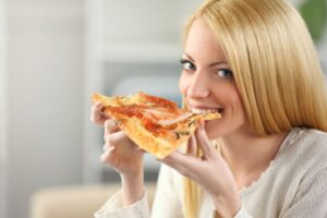 donna che sorride mentre mangia una fetta di pizza