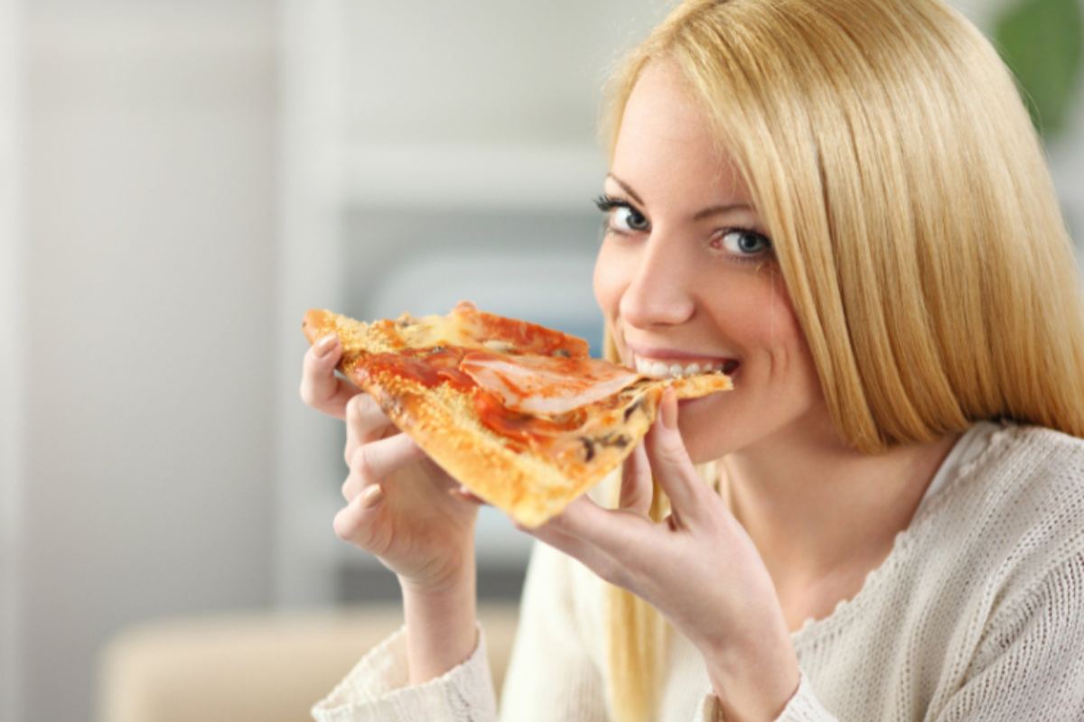 donna che sorride mentre mangia una fetta di pizza