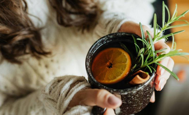 una persona che tiene in mano un bicchiere con il limone e il rosmarino