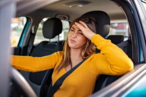 donna alla guida dell'auto preoccupata con una mano sulla fronte e l'altra sul volante
