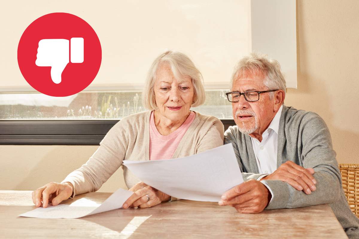 Due pensionati che leggono dei documenti ed in alto a sinistra un pollice in giù