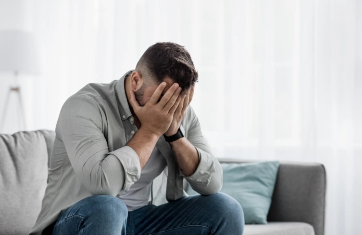 uomo disperato sul divano con le mani in faccia