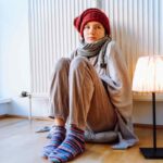 Ragazza imbacuccata seduta davanti al termosifone