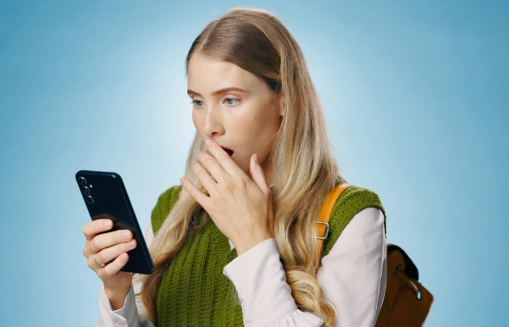 donna con il cellulare in mano con espressione stupita e l'altra mano davanti alla bocca