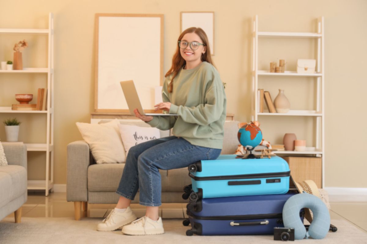 donna seduta sopra delle valigie con il computer aperto in mano