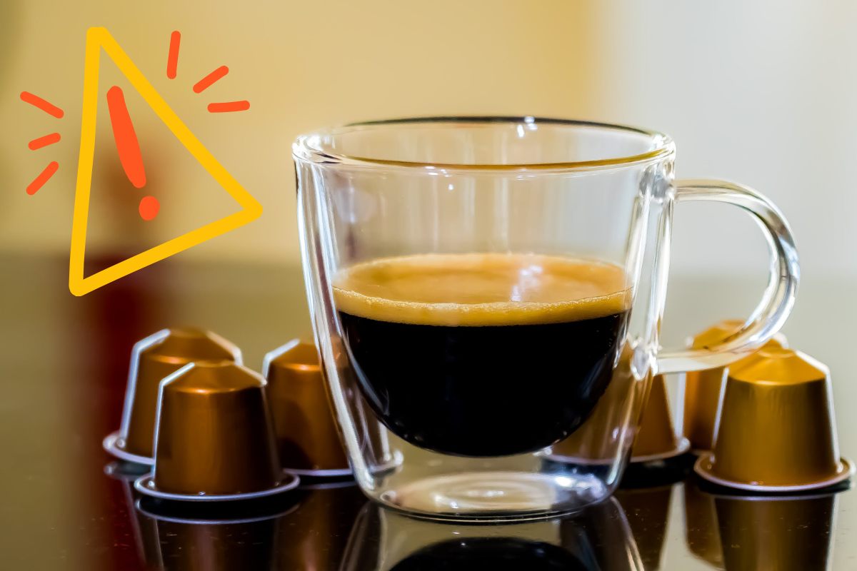 Una tazzina di caffè con attorno delle capsule ed in alto a sinistra un segnale di pericolo