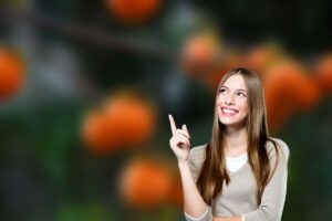 Uno sfondo di un albero di cachi sfocato ed una ragazza in primo piano che lo indica