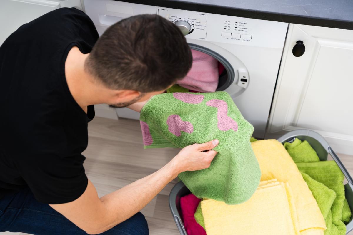 Un uomo che tira fuori dalla lavatrice un panno con macchie di candeggina