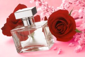 flacone di profumo con accanto delle rose rosse e dei fiori di pesco