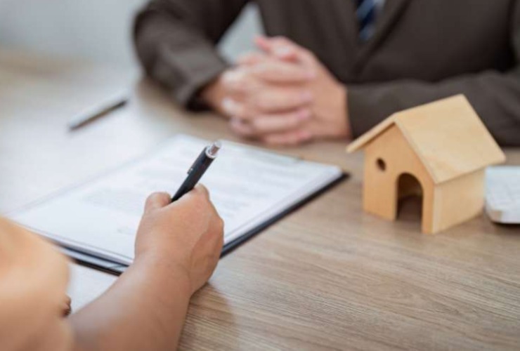 persona che firma, casa in miniatura su una scrivania