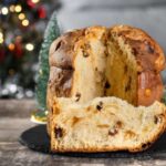 Un panettone tagliato su un tavolo e dietro un albero natalizio