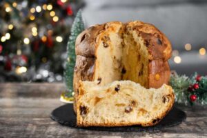 Un panettone tagliato su un tavolo e dietro un albero natalizio