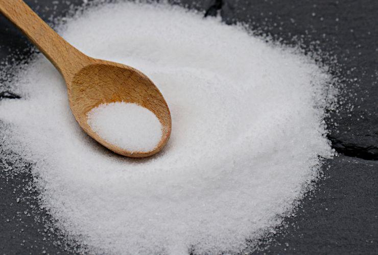 mucchio di sale su sfondo nero e cucchiaino di legno