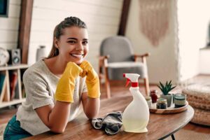 ragazza sorridente seduta con guanti per le pulizie e spruzzino